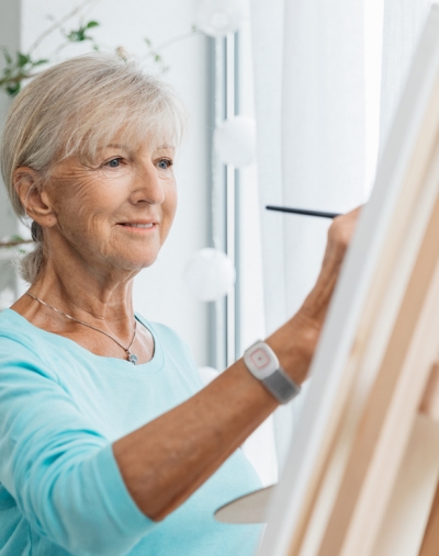 Eine ältere Frau trägt das Notruf-System beim Malen